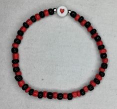 a red and black beaded bracelet with a white heart charm on it's end