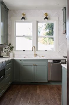 a kitchen with green cabinets and white walls, two windows above the sink is a dishwasher