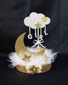 a gold and white cake topper with stars, moon and clouds on it's side