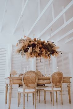 a dining room table with chairs and an arrangement of flowers hanging from the ceiling over it