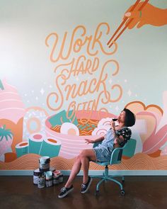 a woman sitting in a chair next to a wall with words on it and some cans