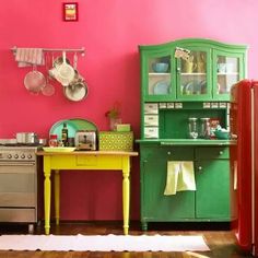 a kitchen with pink walls and green furniture in the center, including a yellow table