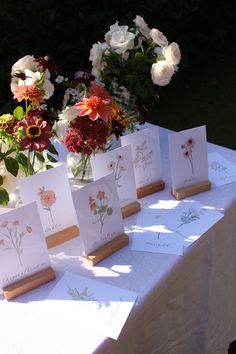 flowers are in vases on top of cards at a table with white and red cloth