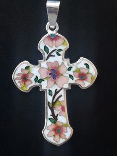 a cross with flowers painted on it is hanging from a chain that's attached to a black surface