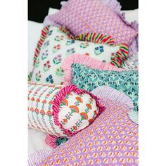 several colorful pillows on a white bed with pink and blue trimmings, all stacked together