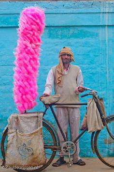 a man standing next to a bicycle with a pink object on it's back