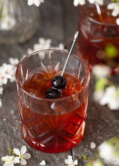 a glass filled with red liquid and an olive on the side, next to flowers