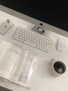 an apple keyboard, mouse and book on a white desk with a cup of coffee