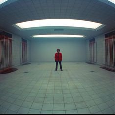 a man standing in an empty room with white tiles on the floor and red curtains