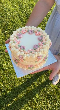 a person holding a cake with flowers on it in their left hand and the other hand is holding another cake