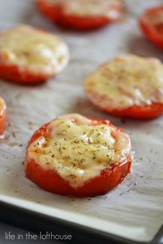 tomatoes with cheese and seasoning sitting on a baking sheet