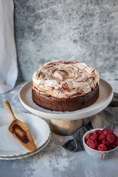 a chocolate cake with white frosting and raspberries in bowls on the side