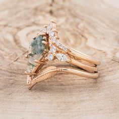 two gold rings with green and white stones on them sitting on top of a piece of wood