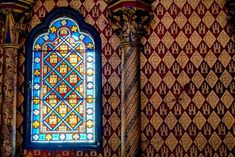 a stained glass window in the corner of a room with red and gold wallpaper