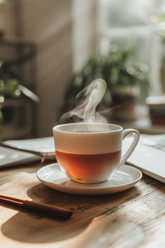 a cup of tea sitting on top of a wooden table next to a laptop computer