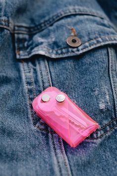 a pink cell phone sitting in the pocket of a jean jacket with two buttons on it