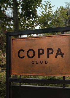 a metal sign that reads coppa club on the side of a fence with trees in the background