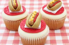 three cupcakes with hot dogs on them are sitting on a checkered tablecloth