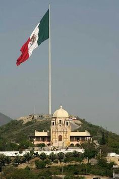 an italian flag flying in front of a building on top of a hill with trees