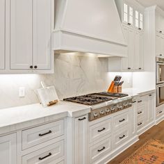 a kitchen with white cabinets and marble counter tops, along with an area rug on the floor