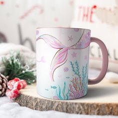 a pink and white coffee mug sitting on top of a table next to pine cones