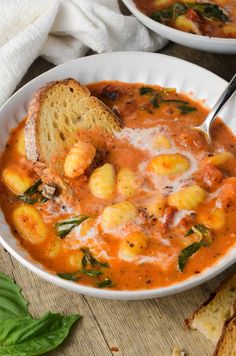 two bowls of soup with bread and spinach on the side, next to each other