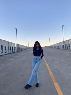 a woman standing in the middle of an empty parking lot wearing high rise jeans and black shoes