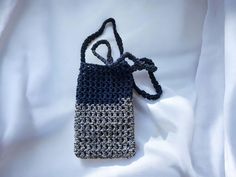 a crocheted bag sitting on top of a white sheet with a black handle