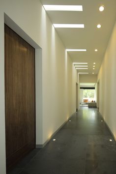 an empty hallway with lights on the ceiling and wooden doors leading to another room in the background