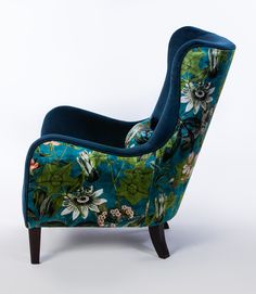 an upholstered chair with blue and green flowers on the back, sitting in front of a white background