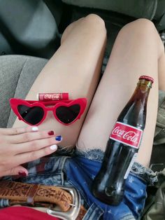 a woman wearing red sunglasses and holding a bottle of coca - cola in her lap