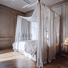 a white canopy bed sitting in a bedroom next to a wooden table and lamp on top of a hard wood floor