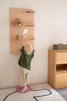 a little boy standing on top of a rug next to a wall mounted book shelf