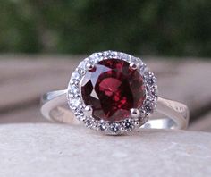 "A round-shaped faceted sparkly Garnet accented with pave-set white crystal on a tapered band handcrafted in Sterling SIlver is a swoon-worthy engagement/promise/anniversary ring. Garnet makes a lovely birthstone ring for those January Birthdays. Wrapped in a box ready for gift giving.(r-halo-garnet). Choose your finish from the drop down menu: Sterling Silver, Rose Gold Plated or 18k Vermeil(gold plated over sterling silver) Gemstone measure 10mm ----> Please note there is an additional fee, Luxury Garnet Jewelry With Halo Setting, Dazzling Ruby Ring With Halo Setting, Dazzling Round Ruby Ring With Halo Setting, Garnet Crystal Ring For Anniversary, Anniversary Garnet Crystal Ring, Ruby Crystal Ring With Accent Stones, Red Cubic Zirconia Crystal Ring, Red Crystal Ring With Center Stone, Round Garnet Ring With Halo Setting