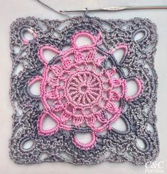 a crocheted square with a pink flower on it and a hook in the middle