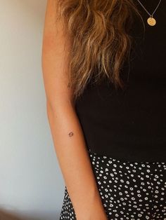 a woman with a small tattoo on her left arm, wearing a polka dot skirt