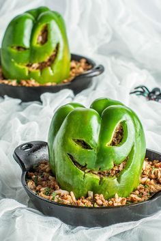 two green peppers with faces carved into them sitting in a skillet on a white cloth