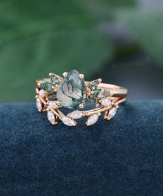 a ring with green and white stones in it on a blue cloth next to a plant