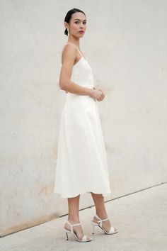 a woman standing in front of a white wall wearing high heels and a halter dress