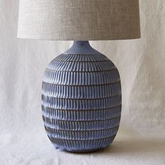 a blue ceramic table lamp with a beige shade on the top and bottom, in front of a white background