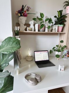 a laptop computer sitting on top of a white desk next to a potted plant