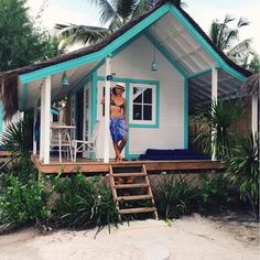 a woman standing on the porch of a small white and blue house with steps leading up to it