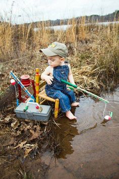 a little boy sitting in the mud with fishing rods and lures on his feet