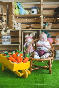 a baby sitting in a chair next to a wheelbarrow filled with carrots