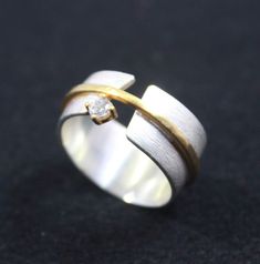 a white and yellow gold ring with a diamond on the top, sitting on a black surface