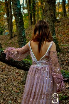 a woman in a long dress walking through the woods