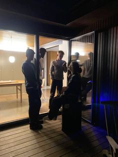 four people standing in front of an open glass door at night, talking to each other