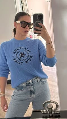 a woman taking a selfie in front of a mirror wearing jeans and a blue sweater