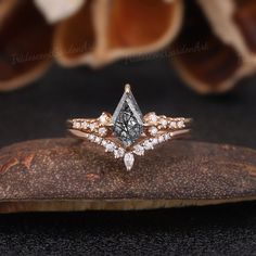 an engagement ring set with two diamonds on top of a piece of wood next to a flower