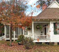 a white house sitting in the middle of a leaf covered yard with trees and bushes